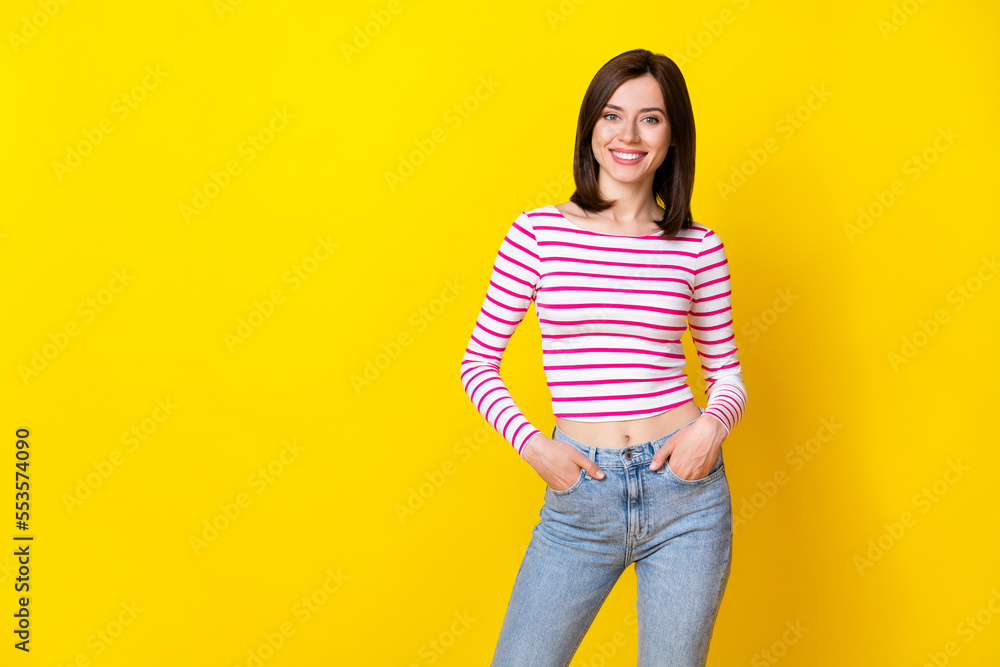 Photo portrait of gorgeous young girl toothy smile confident hold hand pockets wear trendy striped look isolated on yellow color background Photo portrait of gorgeous young girl toothy smile confident hold hand pockets wear trendy striped look isolated on yellow color background