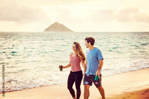 Millennial couple walking along Lanikai Beach with the Mokes Islands in the background; Lanikai, Oahu, Hawaii, USA photo