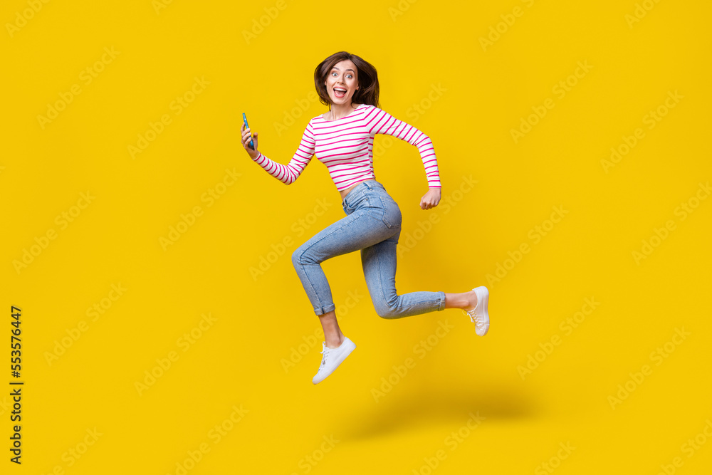 Full length photo of stunning young woman hold telephone run influencer dressed trendy striped clothes isolated on yellow color background