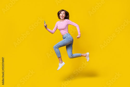 Fototapeta Naklejka Na Ścianę i Meble -  Full length photo of stunning young woman hold telephone run influencer dressed trendy striped clothes isolated on yellow color background
