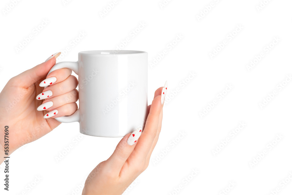 Women's hands hold a mockup of a white empty mug on a isolated background, a cup for your design and logo close-up. White manicure nails with red hearts for Valentine's Day. Women's hands hold a mockup of a white empty mug on a isolated background, a cup for your design and logo close-up. White manicure nails with red hearts for Valentine's Day.