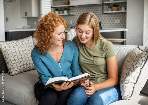 Mother and teenage daughter sitting on a couch at home reading the Bible together; Edmonton, Alberta, Canada