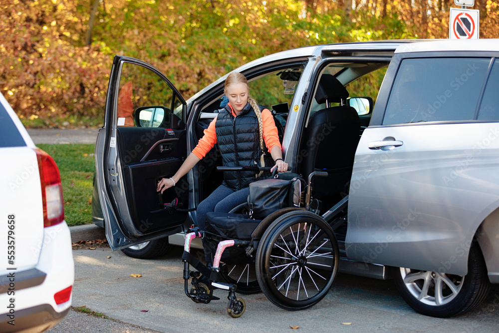Young paraplegic woman moves from her wheelchair to the driver's seat of a car and loads the