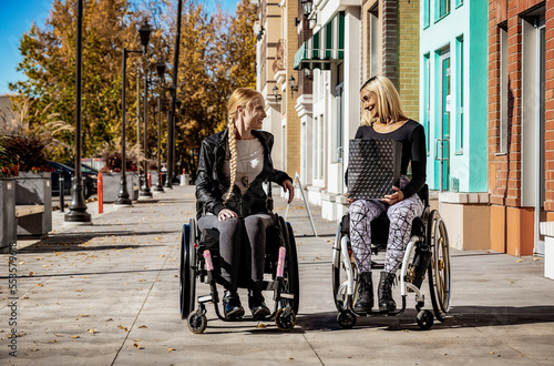 Wallpaper Mural Two young women paraplegics in their wheelchairs visiting together on a walkway on a beautiful fall day, one holding a shopping bag; Edmonton, Alberta, Canada Torontodigital.ca