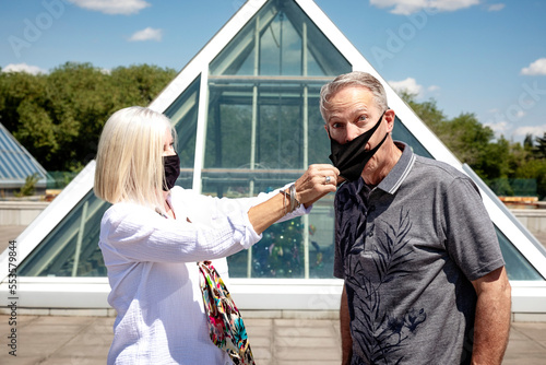 A mature couple stands outside wearing their face masks, the wife pulling the mask off her husband, during the Covid-19 pandemic; Edmonton, Alberta, Canada photo