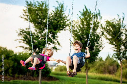 Young girl and boy holding hands while playing on a swing set at a playground; St. Albert, Alberta, Canada photo