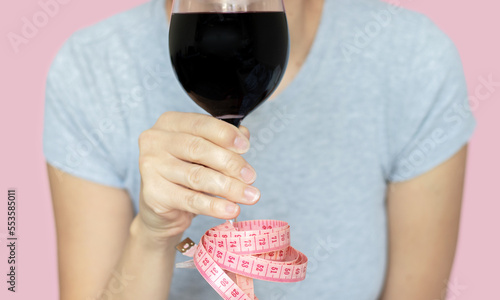 slim woman holding glass with red wine in hand measure tape attached by foot base.celebrating weight loss or drinks and diet nutrition prohibited alcohol consumption.isolated girl pink background