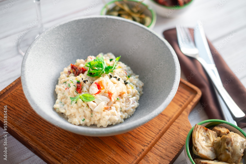 Risotto with crab meat and vegetables is served in a bowl. Dish with rice and seafood on table