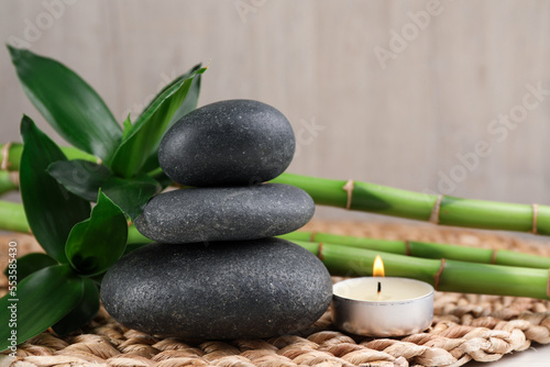 Stacked spa stones, bamboo and burning candle on wicker mat, closeup