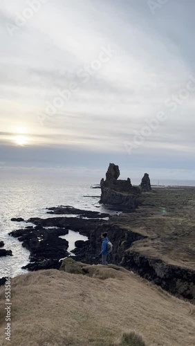 Traveler man walking towards the cliffs over the sea on the Snaefellsnes peninsula in Iceland. Vertical video.