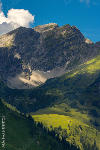Bergpanorama mit steilen Alpen-Hängen und einsamer Berghütte, dramatisches Wetter 