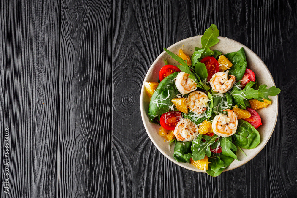 delicious fresh shrimp salad with orange and cherry tomatoes on a black wooden rustic background
