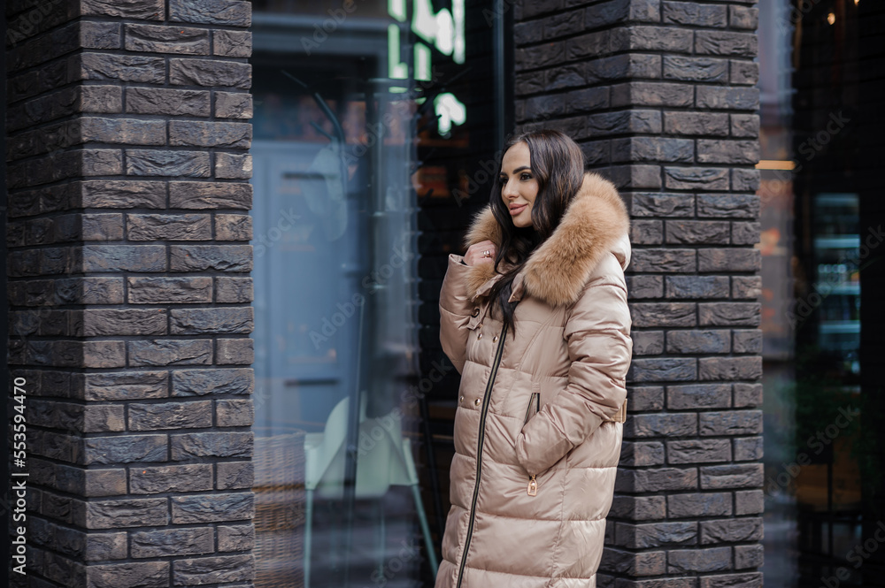 Beautiful young pregnant woman in a brown coat, in the background a brick wall