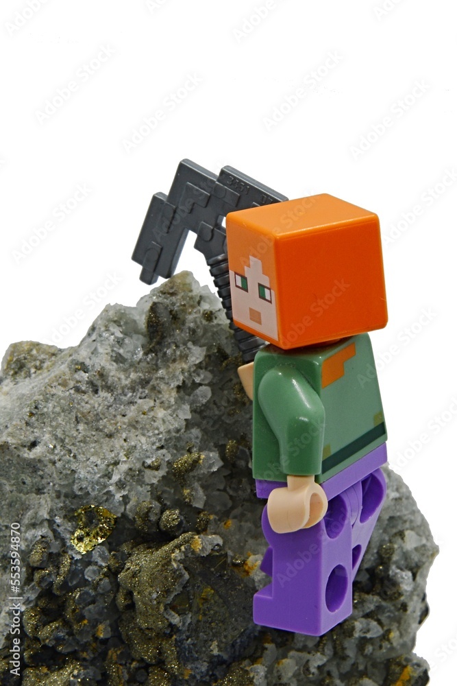 Fototapeta premium LEGO Minecraft figure of Alex with iron pickaxe mining Chalcopyrite mineral rock, white background.