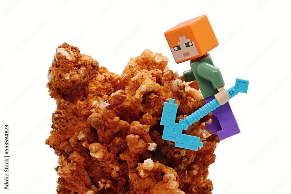Fototapeta premium LEGO Minecraft figure of Alex with diamond pickaxe climbing on Calcite (Calcium Carbonate) stone, white background.