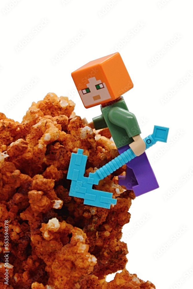 Naklejka premium LEGO Minecraft figure of Alex climbing on orange Calcite mineral rock with diamond pickaxe, white background. 