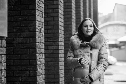 Beautiful young pregnant woman in a brown coat, in the background a brick wall