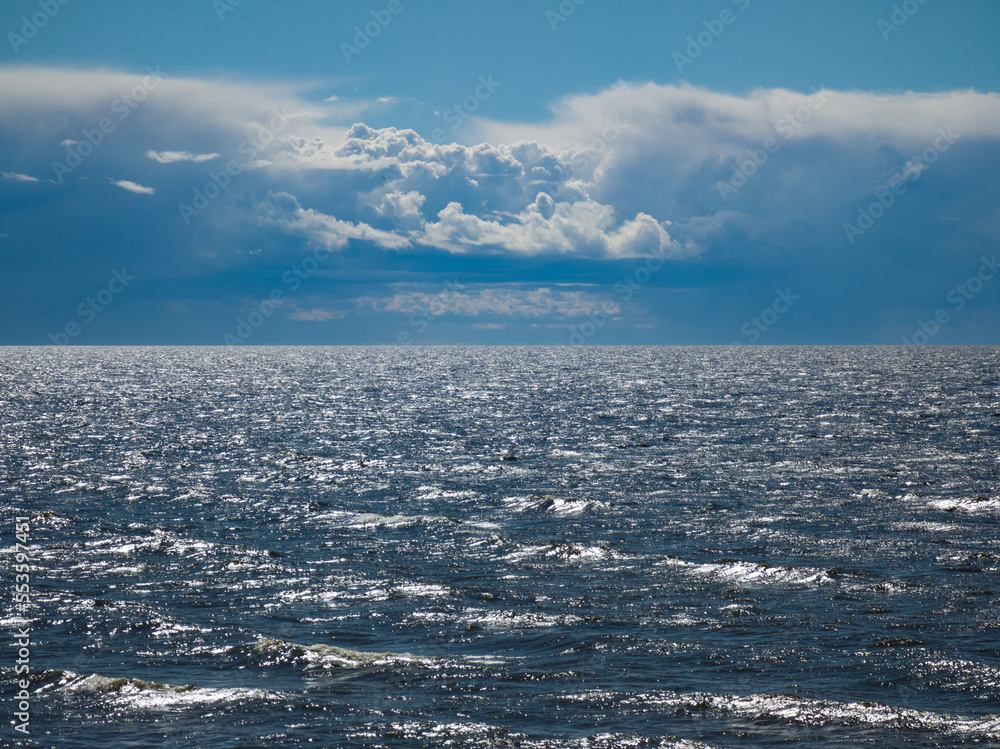 Beautiful seascape. Cloudy sky. Reflection of sunlight on sea waves.