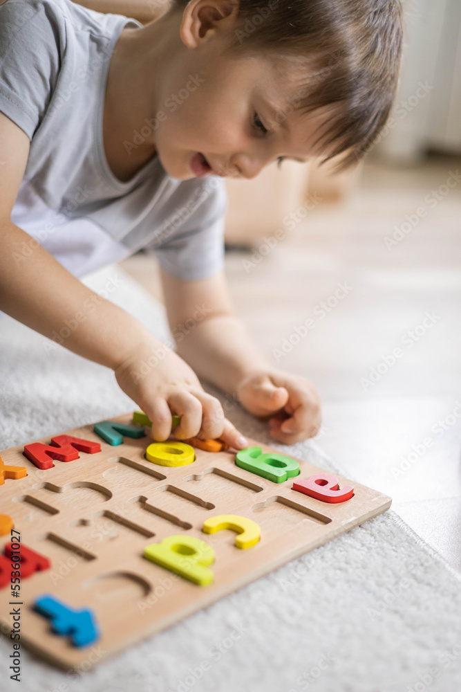 Male kid playing with wooden eco friendly alphabet letters board on table top view intellectual game Male kid playing with wooden eco friendly alphabet letters board on table top view intellectual game