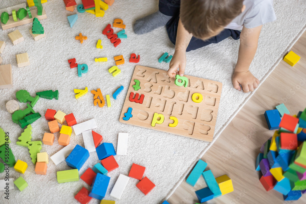 Male kid playing with wooden eco friendly alphabet letters board on table top view intellectual game Male kid playing with wooden eco friendly alphabet letters board on table top view intellectual game