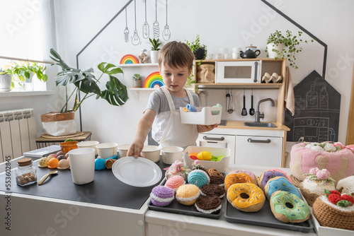 Male baby chef in apron posing at childish kitchen cafe public catering food sweet toys imitation