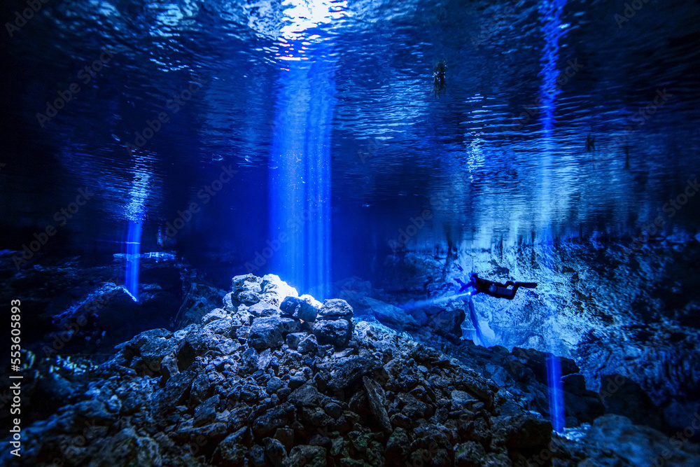 A cave diver descends into a cave system with light rays