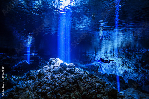 A cave diver descends into a cave system with light rays penetrating the water in the background. photo