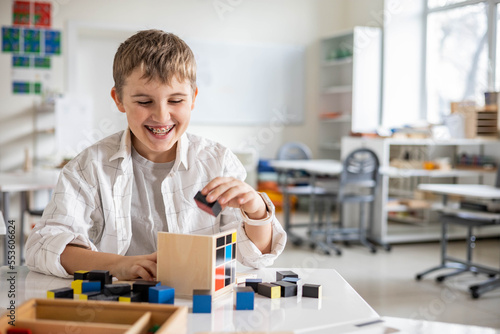 Photos Happy male kid assembling Montessori material trinomial cube at school classroom