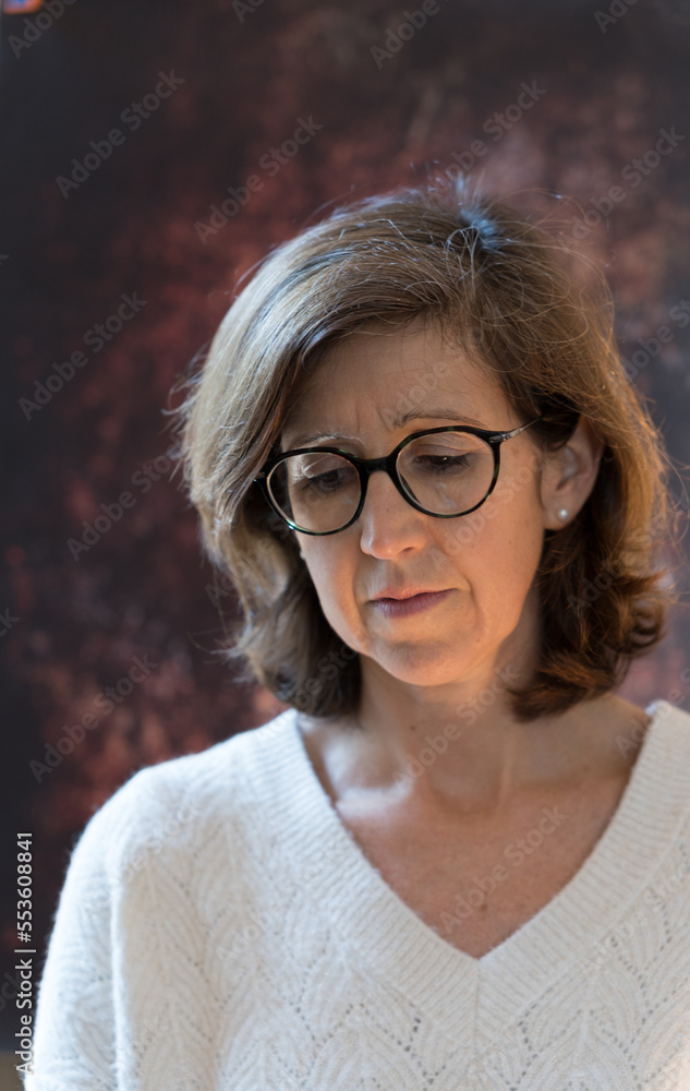 portrait of a 50 year old woman on a dark brown background who looks worried or annoying portrait of a 50 year old woman on a dark brown background who looks worried or annoying
