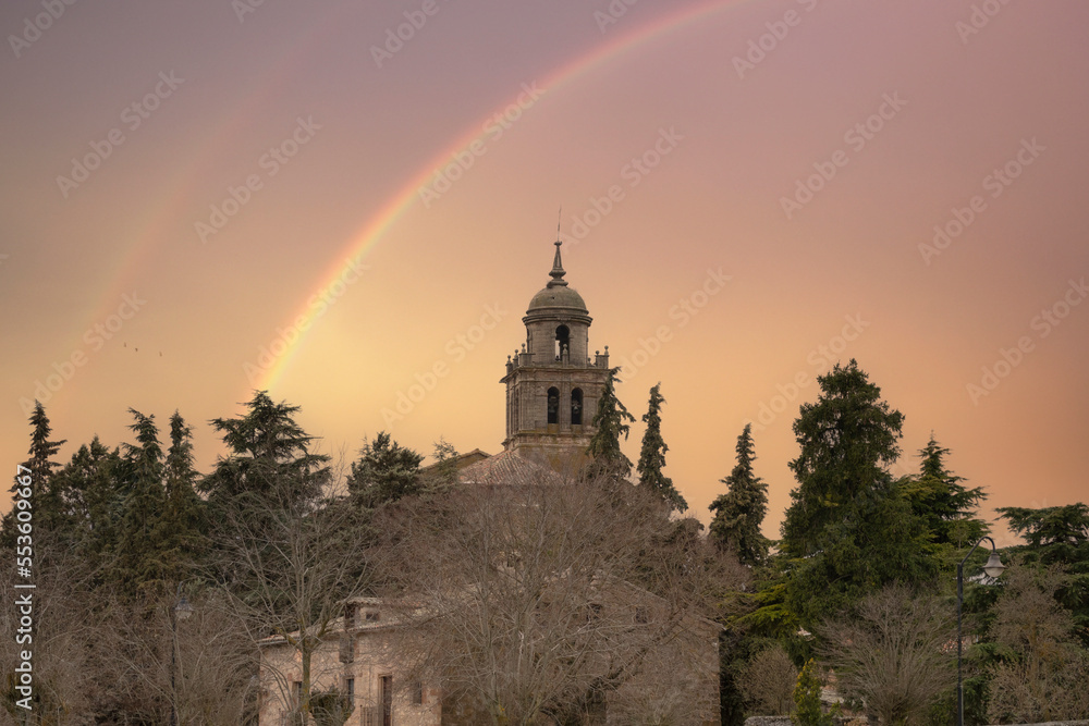 Town of Medinaceli and view of the collegiate church in Soria after the passing of the storm leaving a reddish sunset and a rainbow in the sky, Spain