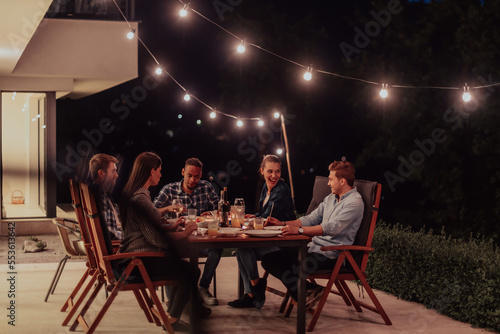 A group of young diverse people having dinner on the terrace of a modern house in the evening. Fun for friends and family. Celebration of holidays, weddings with barbecue.