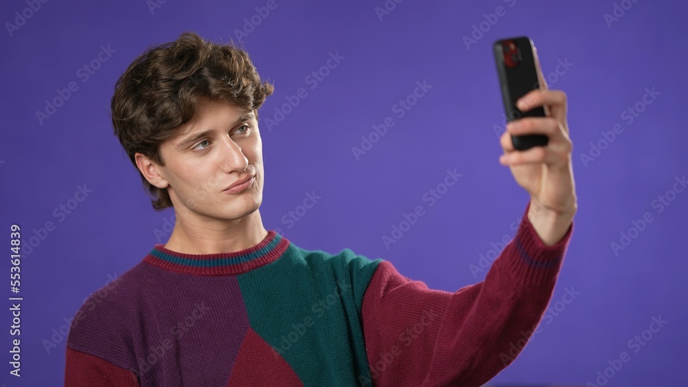 Portrait of happy smiling young guy 20s in sweater taking selfie with mobile cell phone conducting pleasant conversation isolated on purple background studio. Portrait of happy smiling young guy 20s in sweater taking selfie with mobile cell phone conducting pleasant conversation isolated on purple background studio.