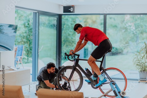 A cameraman filming an athlete riding a triathlon bike on a simulation machine in a modern living room. Training in pandemic conditions.