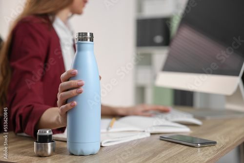 Woman holding thermos bottle at workplace, closeup. Space for text photo