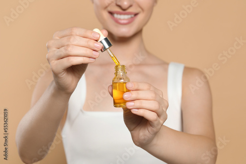Young woman with bottle of essential oil on beige background, closeup