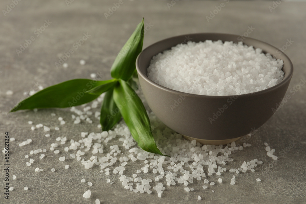 Bowl of natural sea salt and green leaf on grey table