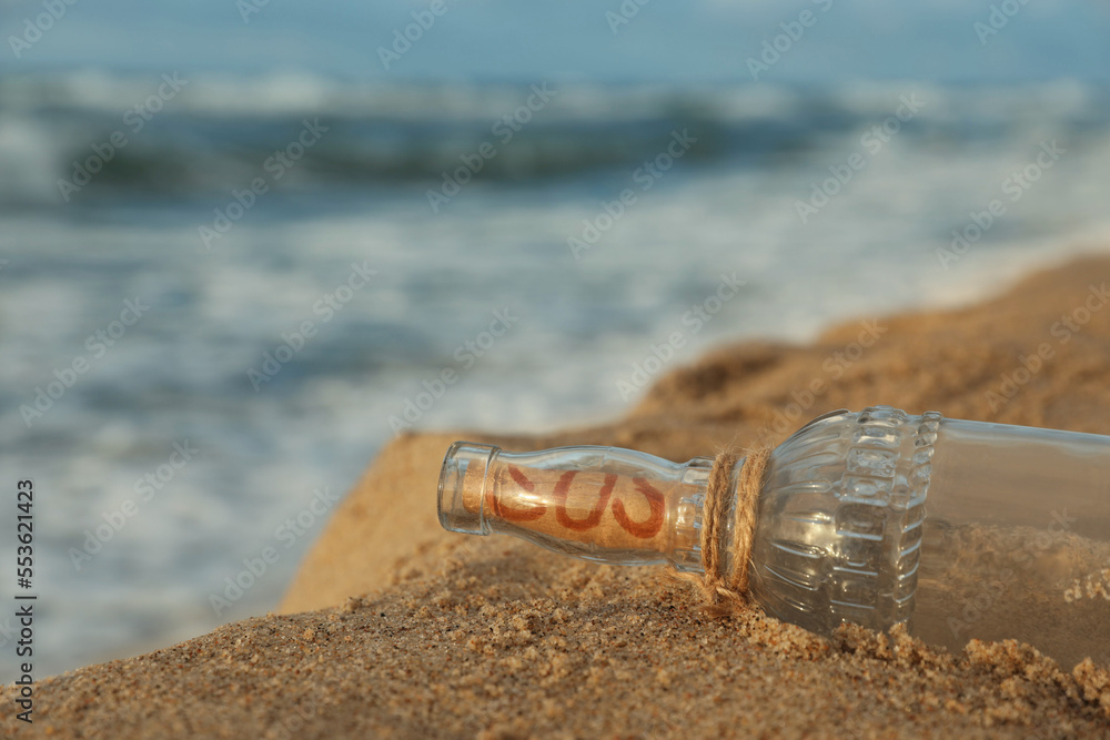 Glass bottle with SOS message on sand near sea, space for text Glass bottle with SOS message on sand near sea, space for text