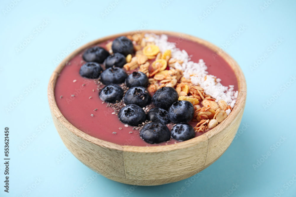 Bowl of delicious fruit smoothie with fresh blueberries, granola and coconut flakes on light blue background, closeup Bowl of delicious fruit smoothie with fresh blueberries, granola and coconut flakes on light blue background, closeup