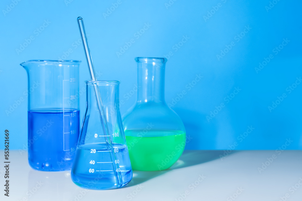 Glass flasks with colorful liquids on white table against light blue background. Space for text Glass flasks with colorful liquids on white table against light blue background. Space for text
