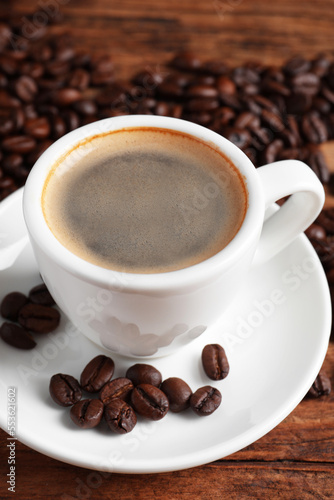 Cup of hot aromatic coffee and roasted beans on wooden table, closeup