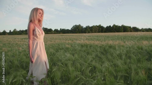 Blonde-haired, caucasian woman enjoying natural environment of countryside. Pretty, charming lady in the elegant, white dress walking along wheat field. High quality 4k footage
