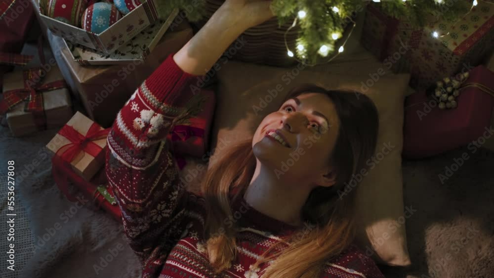 A beautiful girl of European appearance is lying under a Christmas tree. Around the Christmas tree, there are many gifts for the whole family A beautiful girl of European appearance is lying under a Christmas tree. Around the Christmas tree, there are many gifts for the whole family