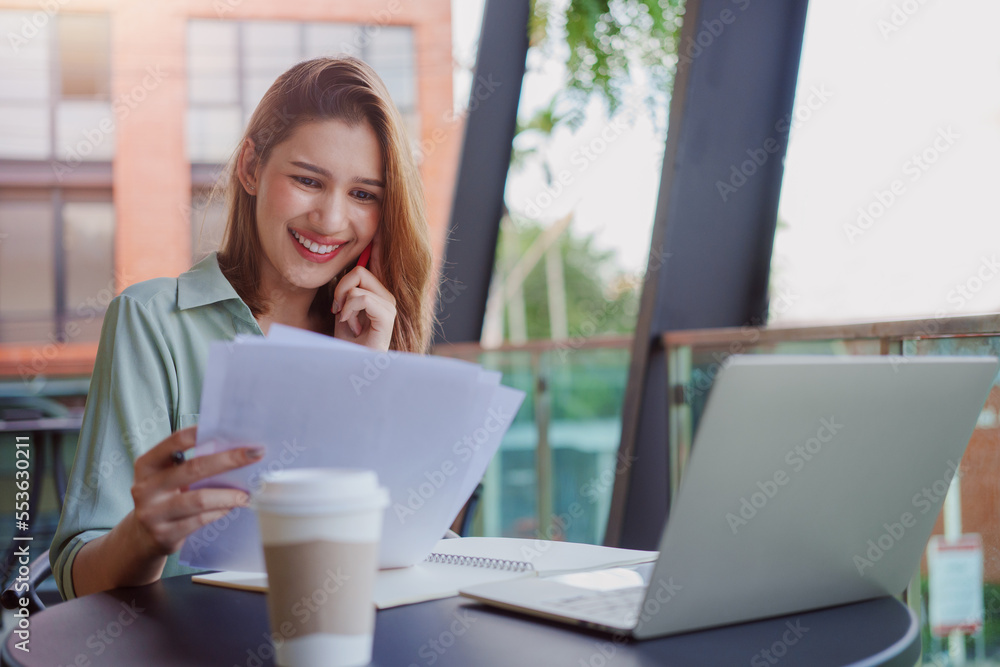 Young businesswoman working with papers and talking on mobile phone, reading financial documents while sitting at cafe. Young businesswoman working with papers and talking on mobile phone, reading financial documents while sitting at cafe.