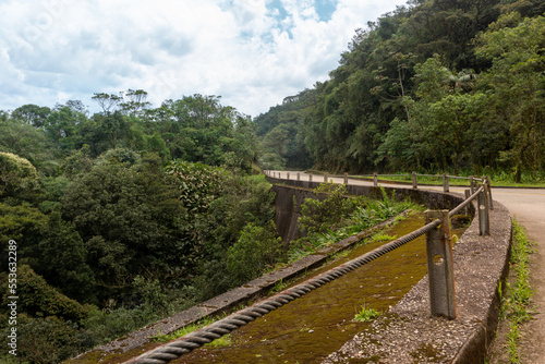 Sharp curve of an old inactivated road that connects the cities of Santos and Sao Paulo. Path surrounded by nature and with a rusty guard rail on the sides. part of the State Park Caminhos do Mar