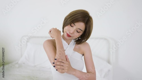 Portrait beauty smiling asian woman applying lotion to arm hand touch skin during her morning routine. Cute asian girl. Skincare body lotion, beauty clinic skincare spa indoors woman lifestyle concept