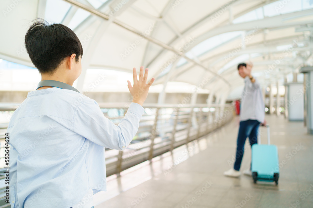 Asian little boy waves a hand and says goodbye to his father at the airport or railway terminal before father leaving. Asian little boy waves a hand and says goodbye to his father at the airport or railway terminal before father leaving.