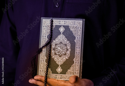 Man Holding Quran. Islamic Background. Arabic on the cover translated with Quran, Muslim man hands holding Quraan with praying beads photo