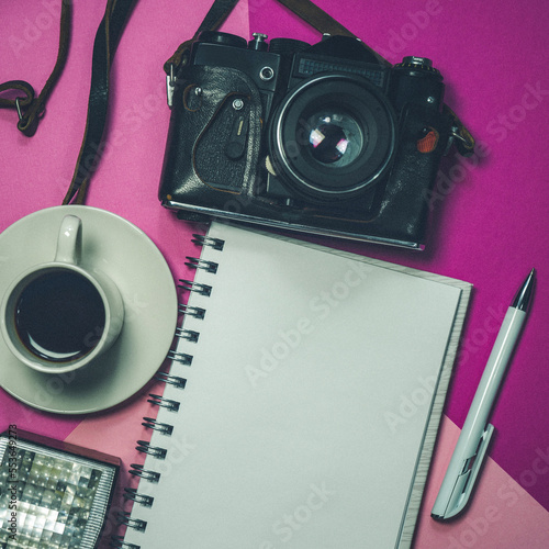 An old camera, a notebook and coffee. Top view of the business table. A retro camera, a notebook and a cup of coffee on the table. Camera, notebook. Space for text. Space for copying. Selective focus.