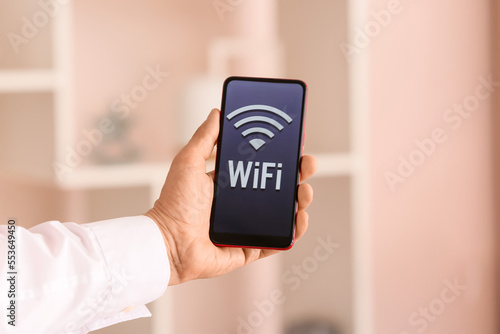 Man holding mobile phone with WiFi symbol in light room, closeup