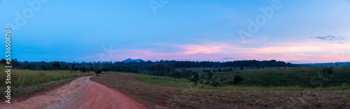 Panoramic view of gravel road in countryside with meadow at sunset